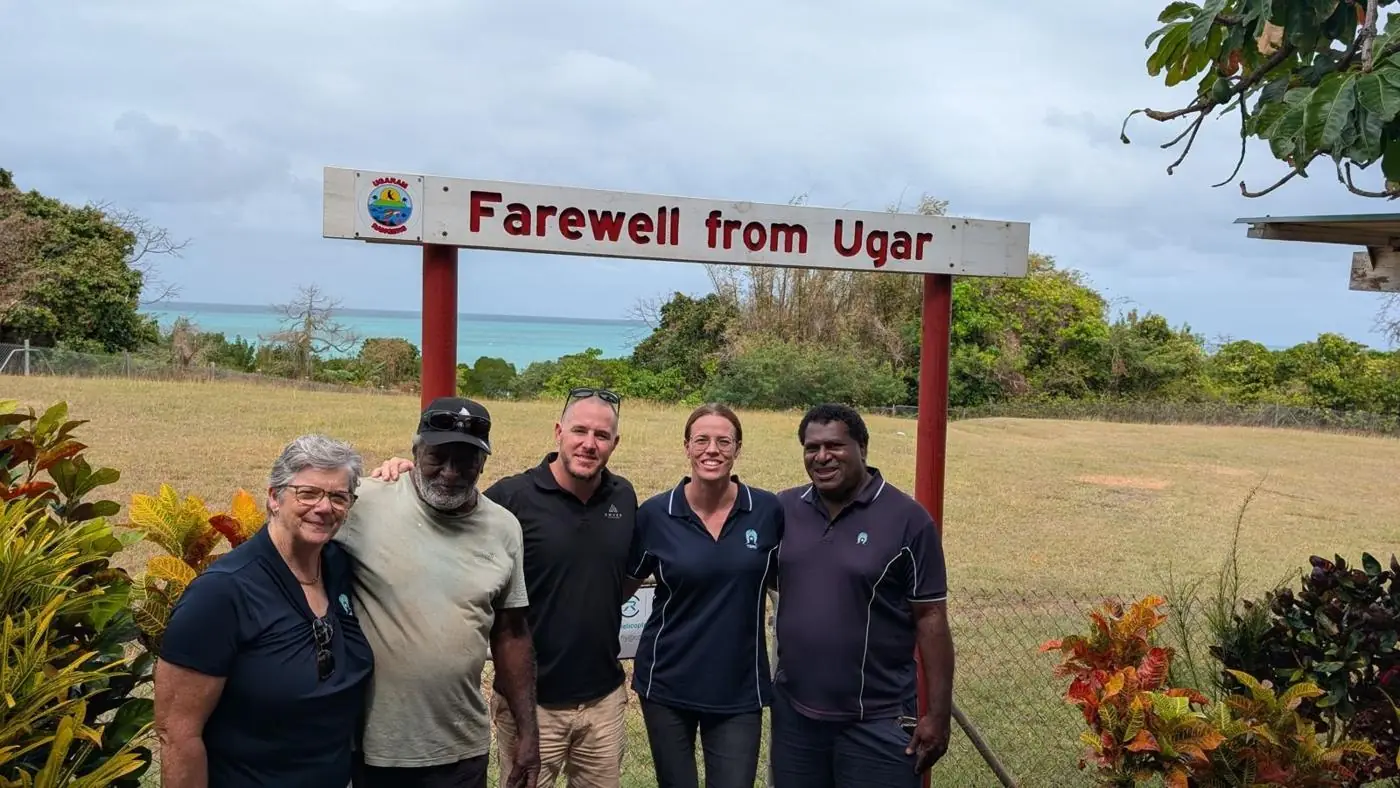 Emver team and community members beside the Farewell from Ugar sign