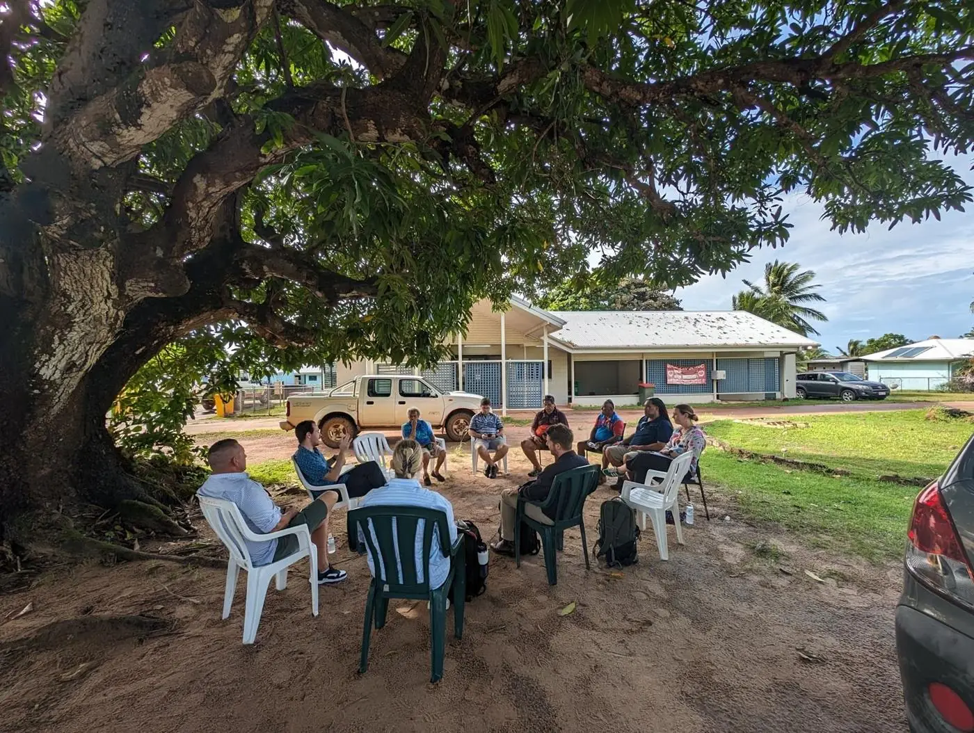 Staff consultation held outdoors under a large tree on Badu Island